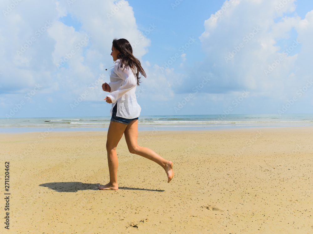 Woman runs on the beach against the background of sea of clouds, in a light white shirt Woman runs on the beach against the background of sea of clouds, in a light white shirt