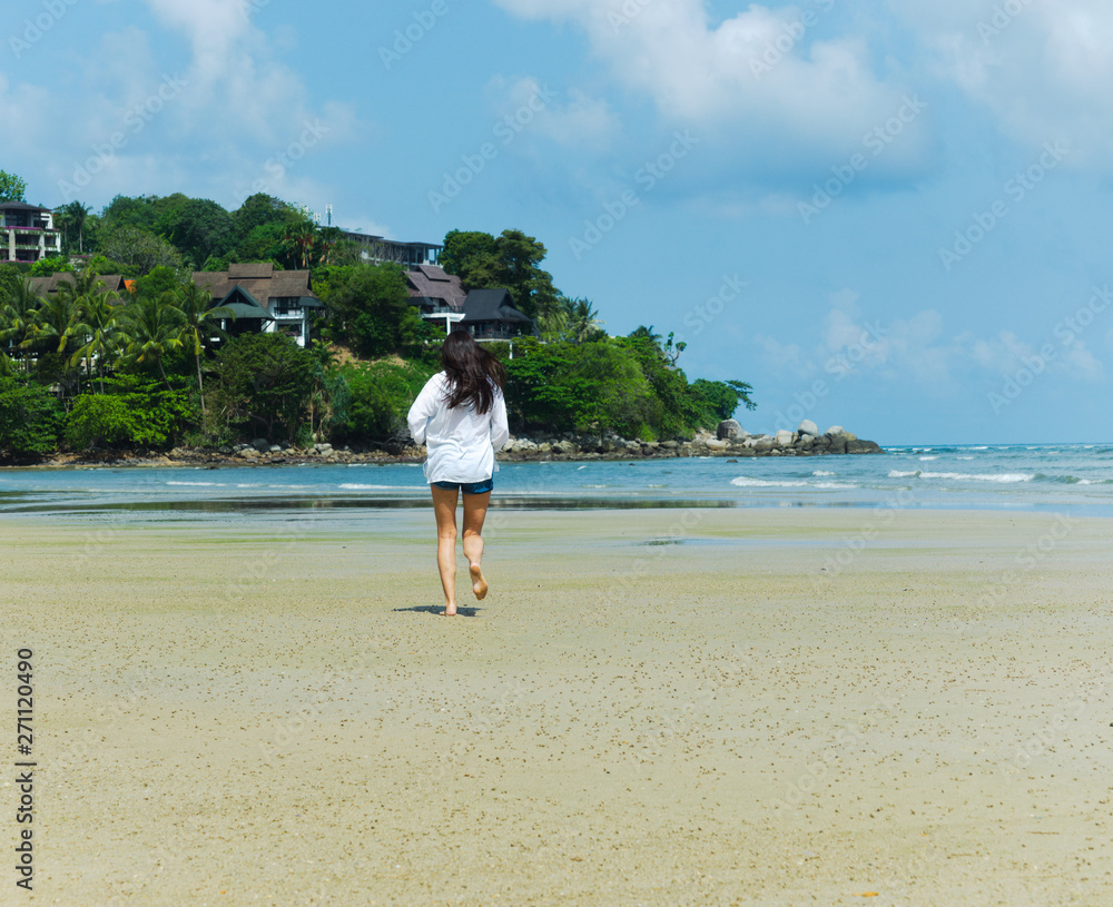 Woman run into the distance on the beach. Back view of woman in a white shirt on the beach Woman run into the distance on the beach. Back view of woman in a white shirt on the beach