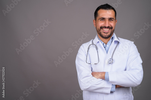 Handsome bearded Persian man doctor against gray background