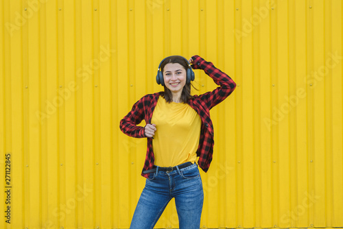 Happy girl listening to music on the street over yellow background
