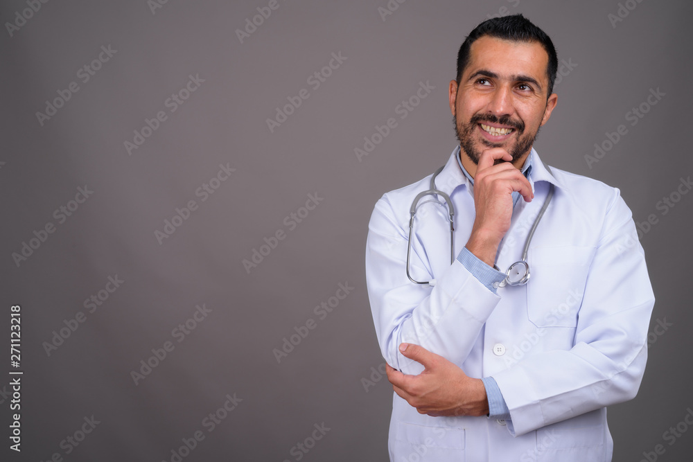 Handsome bearded Persian man doctor against gray background