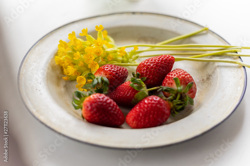 Enameled vintage plate with ripe strawberries and yellow flowers
