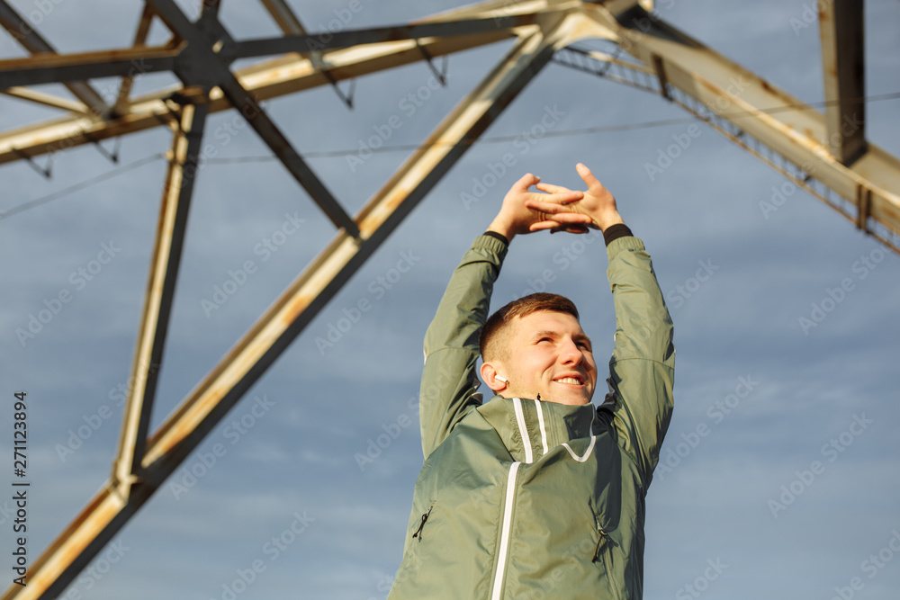 The young man raising his hands up during exercises at the background of the blue sky