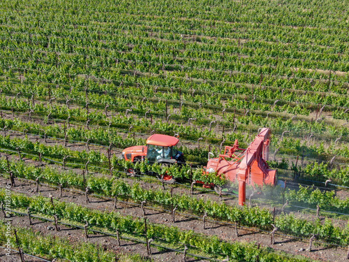 Farm tractor spraying pesticides & insecticides herbicides over green vineyard field. Napa Valley, Napa County, California, USA photo