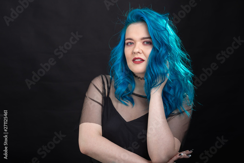 Style, fashion and hair concept - close-up portrait of young woman in black dress with blue hair on black background