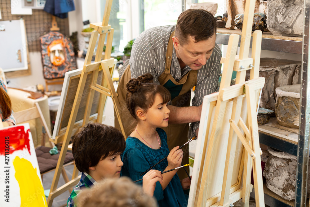 Obraz premium Art teacher speaking with boy and girl while coloring pictures
