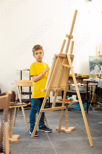 Little boy standing near drawing easel with painting brush