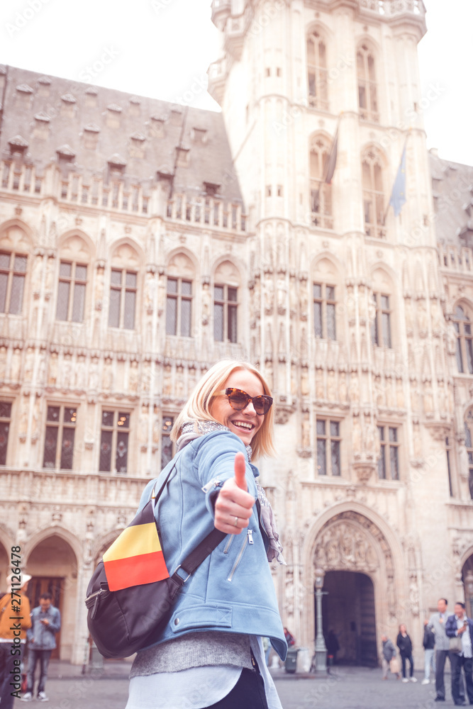 Young happy cheerful woman showing thumb up against the backdrop of the Grand Place in Brussels, Belgium