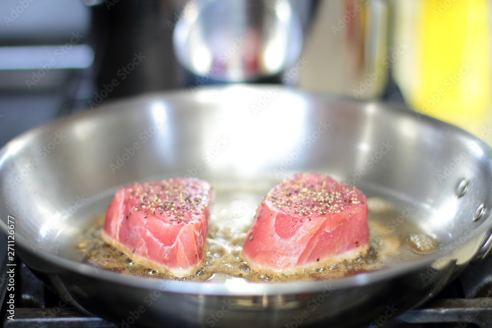 Ahi tuna steaks searing in a stainless steel pan on a gas stove.