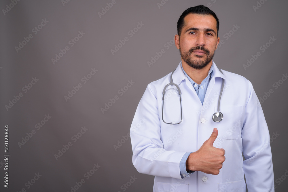 Handsome bearded Persian man doctor against gray background Handsome bearded Persian man doctor against gray background