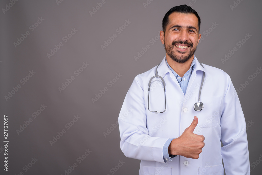 Handsome bearded Persian man doctor against gray background Handsome bearded Persian man doctor against gray background