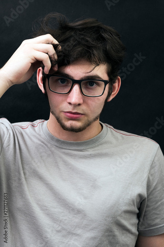 Studio shot of a young handsome guy with gray t-shirt wears glasses on the black background.