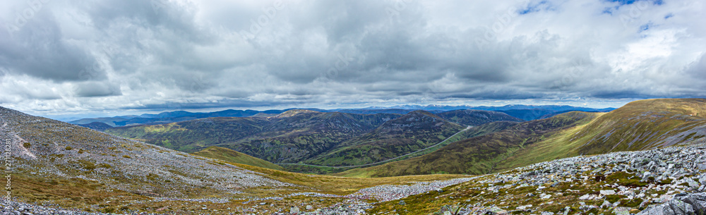 A panorama view of a Scottish mountain valley with a road and mountain range under a stormy huge white clouds sky A panorama view of a Scottish mountain valley with a road and mountain range under a stormy huge white clouds sky