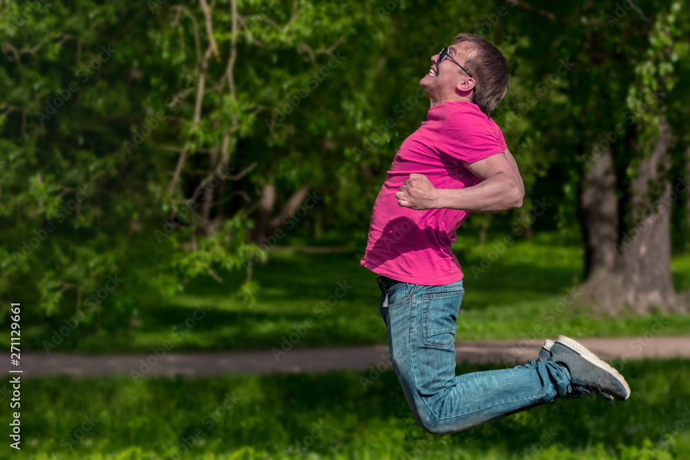 Handsome, sporty guy jumping in the park. Young man in pink t-shirt.