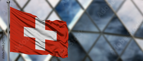 Switzerland flag waving in the wind against blurred modern building. Business concept. National cooperation theme.