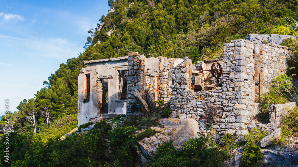 Ruins of an old house with stone brick walls, built next to the Doria Castle, in Porto Venere, La Spezia, Italy. Derelict building with a caved roof in a mountain landscape background.