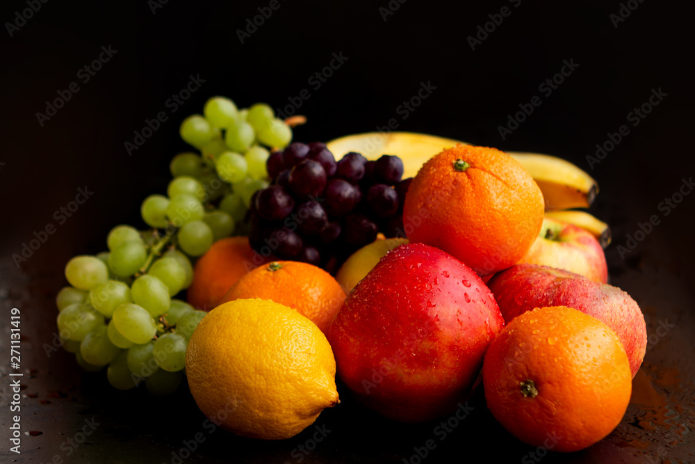 Beautiful juicy fruits on a black wet background: apples, grapes, oranges, bananas, copy space, close-up Beautiful juicy fruits on a black wet background: apples, grapes, oranges, bananas, copy space, close-up