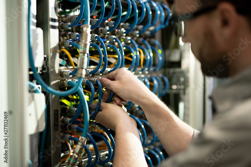 Close-up of busy server support specialist inserting cables into hubs and examining connectivity while repairing supercomputer