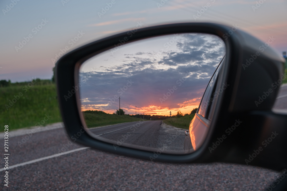 Beautiful summer sunset reflected in the side mirror of the car. View from the car window on the road. Summer landscape in the mirror of the car
