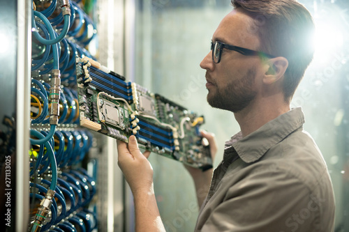 Fotografie Serious skilled young bearded server installation specialist in glasses holding