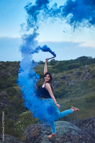 woman looking in camera with blue color smoke bomb on top of mountain