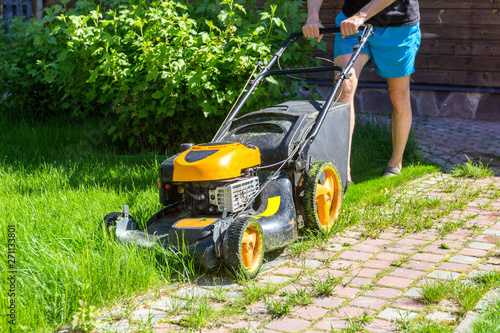 Man mows grass with lawn mower on sunny morning in garden.