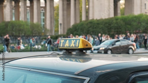 Checkered and taxi sign on the roof of the car close up. City street, day.