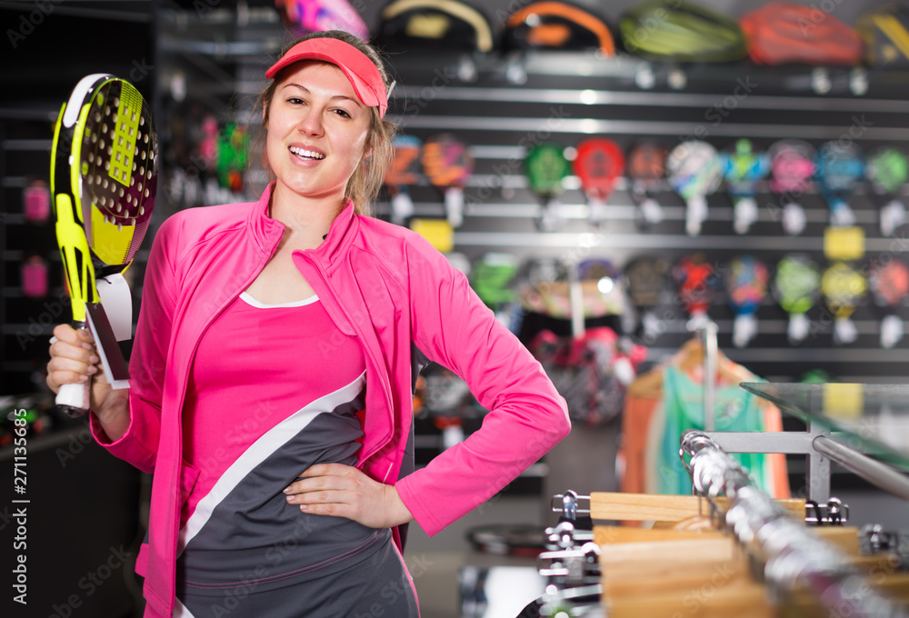 Sporty smiling woman in uniform is holding new racket for padel in the store
