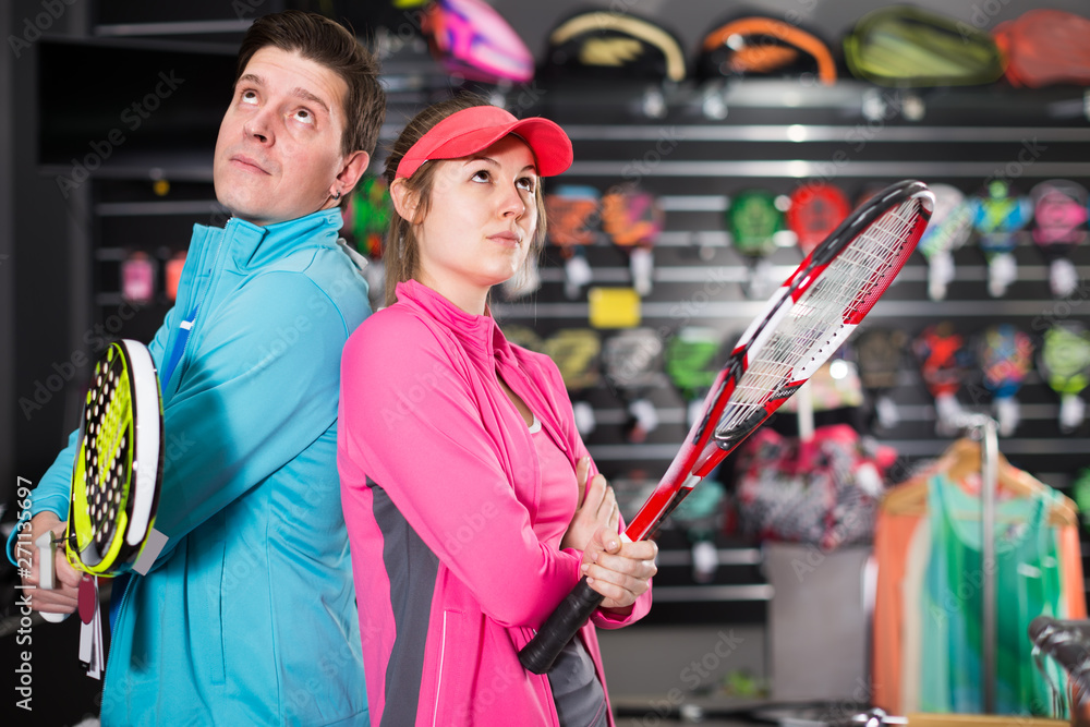 cheerful female with male are standing in sportwear with new racket for padel and tennis in the speciality store