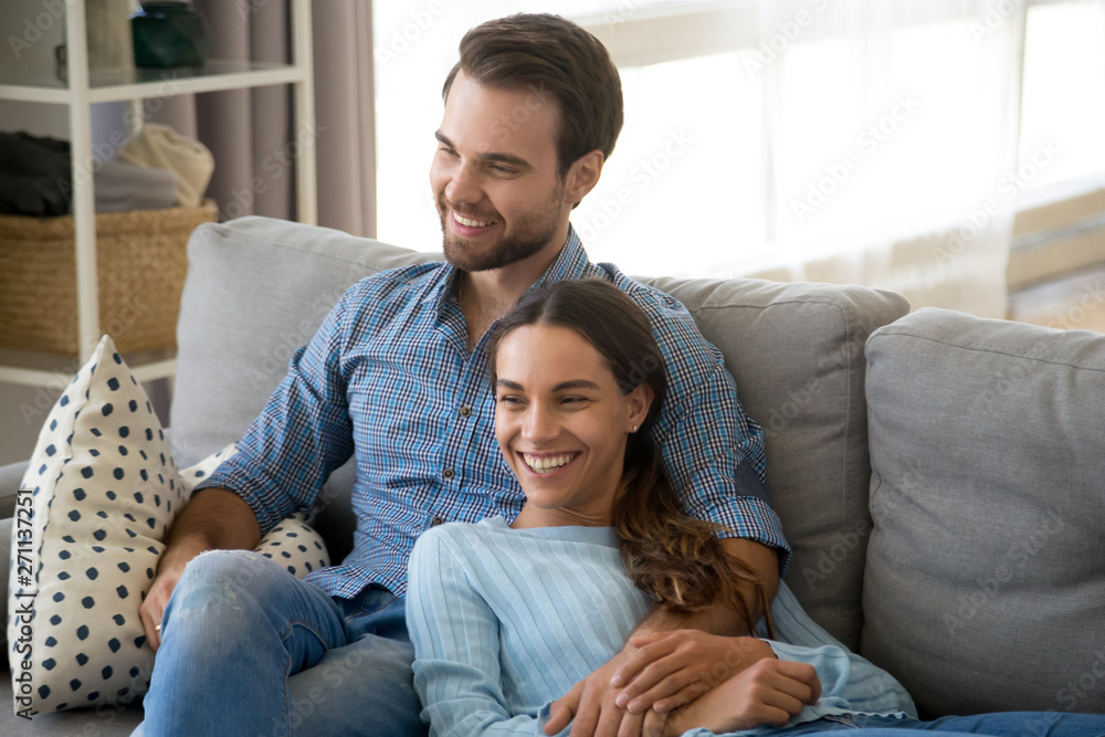 Smiling couple relax on couch cuddling at home
