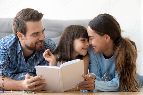 Loving parents enjoy relaxing reading with little daughter