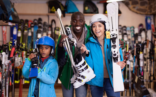 Smiling young African man and European woman with preteen son standing with purchased ski equipment in shop