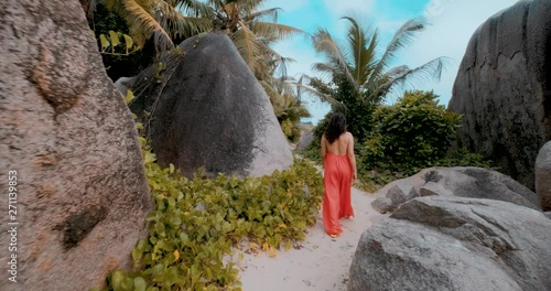 Beautiful Woman Walking on the Beach in Seychelles La Digue, wearing a red dress in 4K UHD. Seychelles La Digue Island Rocky Beach with Palm trees.