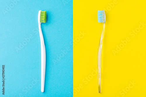 Two plastic toothbrushes on a pastel blue and yellow background, flat lay style
