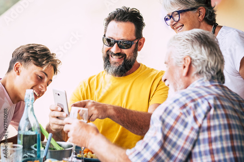 Adult and senior people with a teenager enjoying a funny picture on the mobile phone. Group of family generation. Bright background. BBq time