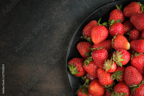 Fresh farm strawberries on a dark plate on a black background.