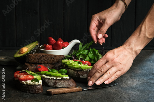 Healthy breakfast sandwich with avocado, cheese, strawberries, herbs and seeds on a dark background. An idea for bruschetta or for a healthy snack. Healthy vegan breakfast.