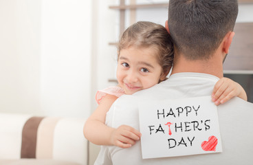 little girl hugs his father and shows happy fathers day card