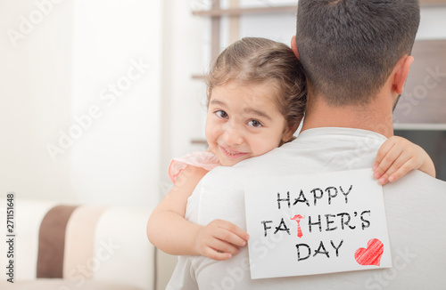 little girl hugs his father and shows happy fathers day card