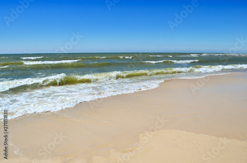 Sea waves wash the clean sandy beach. Landscape on a wild beach. The sea in the summer.