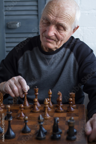 An old man is sitting in front of a chessboard, thinking and making the first move in the game
