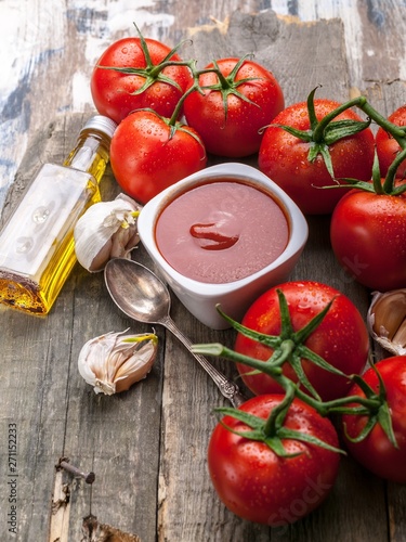 Ketchup or tomato sauce, olive oil, garlic and fresh tomatoes on a branch against a rustic background.