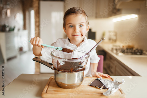 Young boy tastes melted chocolate in a bowl