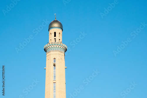 The Golden minaret of the mosque. Muslim symbol on blue sky background. Crescent. Sunset. The concept of religion.