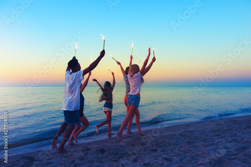 Happy smiling friends running at the beach with sparkling candles