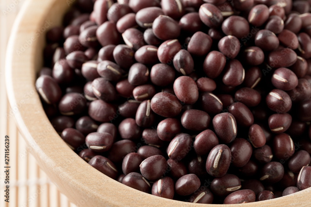 Raw, uncooked, dried adzuki (red mung) beans in wooden bowl on bamboo mat background Raw, uncooked, dried adzuki (red mung) beans in wooden bowl on bamboo mat background