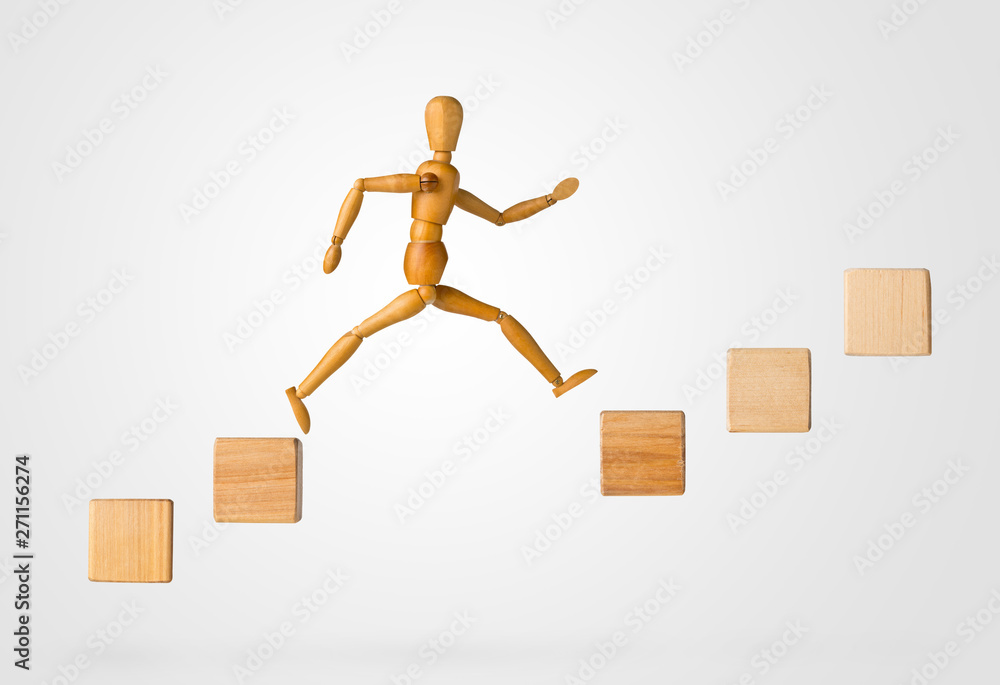 Wooden stick figure jumping from one wooden block on rising steps to the next - achievement, career or objective concept on white Wooden stick figure jumping from one wooden block on rising steps to the next - achievement, career or objective concept on white