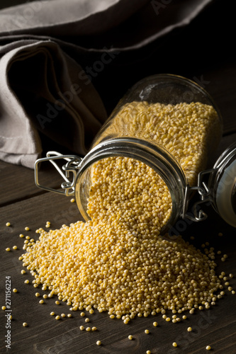 Pile of golden millet, a gluten free grain seed, in glass storage jar on dark table background