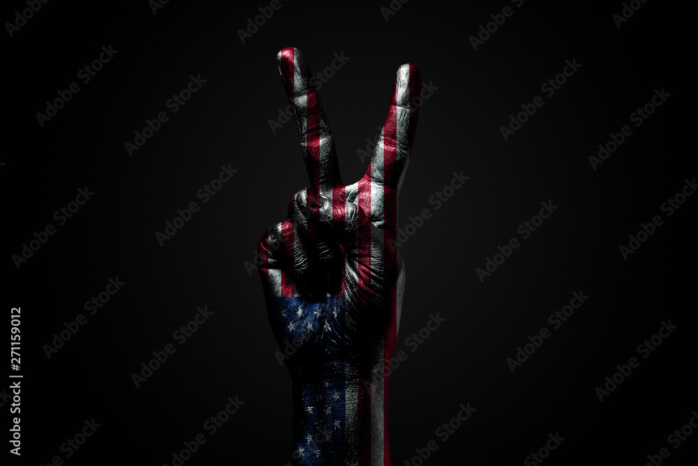 A hand with a drawn USA flag shows an PEACE sign, a symbol of peace, friendship, greetings and peacefulness on a dark background. A hand with a drawn USA flag shows an PEACE sign, a symbol of peace, friendship, greetings and peacefulness on a dark background.