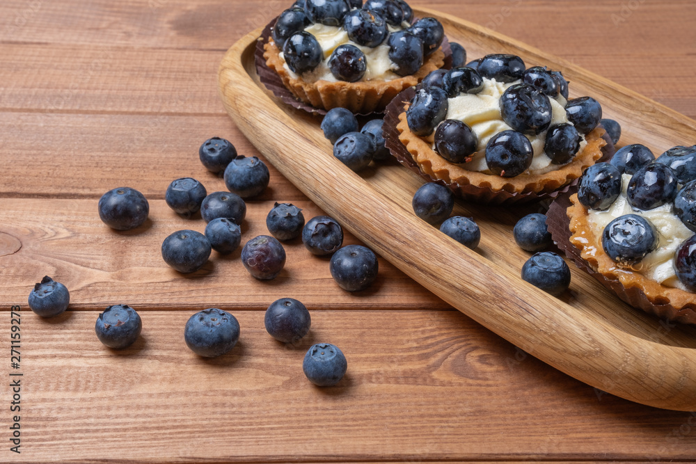 three bilberry tartlet on a wooden plate on the table, bilberry baked shells, fruit cupcake with blueberry three bilberry tartlet on a wooden plate on the table, bilberry baked shells, fruit cupcake with blueberry